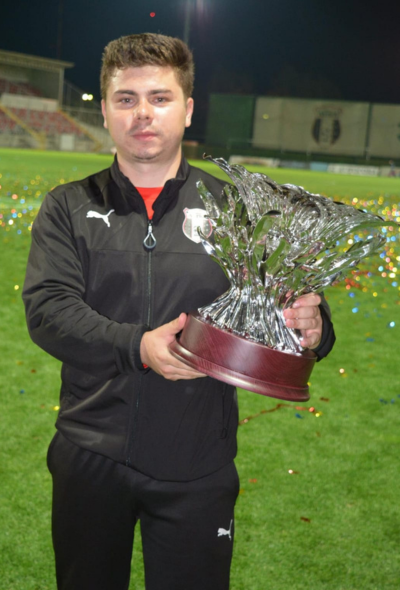 Kinetoterapeut ținând un trofeu pe terenul de fotbal, simbol al excelenței în recuperare sportivă.